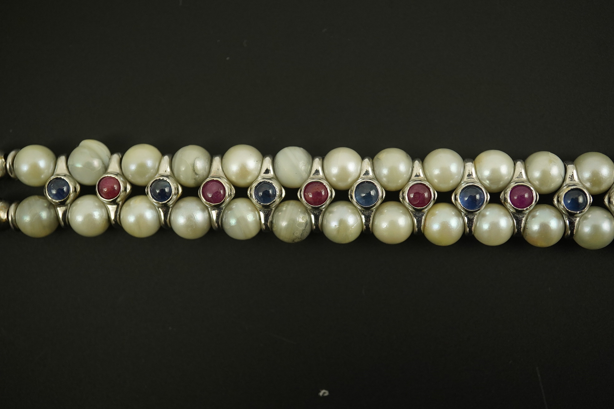 A late 20th century 18k white gold and two row cultured pearl bracelet, set with single row of cabochon rubies and sapphires